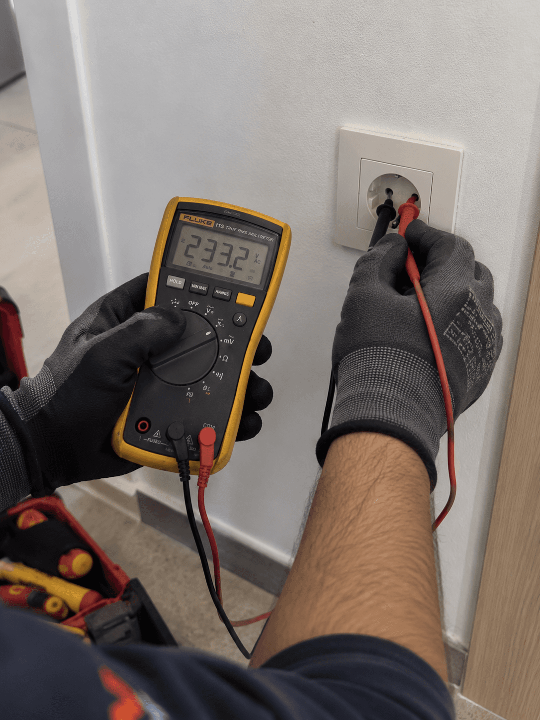 Électricien mesurant la tension d'une prise murale au multimètre